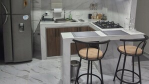 A modern kitchen with a marble floor, wooden cabinets, a built-in island with stools, and pendant lighting.