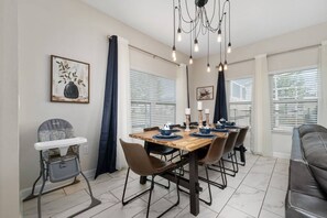 A dining area with a wooden table, chairs, a high chair, and a chandelier. - 5BR Championsgate Home With Pool & Water Park (Davenport)
