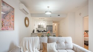 A living room with a sofa, a coffee table, a dining table with chairs, a kitchen area with appliances, and a hallway leading to a bedroom. - Group-Friendly Old Port Suite | Parking | Sleeps 6 (Montreal)