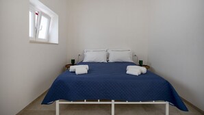 Una cama individual con un edredón azul, almohadas blancas y dos toallas dobladas sobre una estructura metálica blanca.