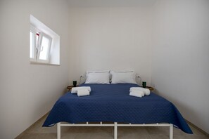 A single bed with a blue quilt, white pillows, and two folded towels on a white metal frame. - Spacious double bedroom with living area and private bathroom, ideal for two, located within Trulli Italia, a complex of trulli with a shared garden. Surrounded by greenery, the accommodation is located in Selva di Fasano, a quiet and verdant hillside ha (Selva di Fasano)