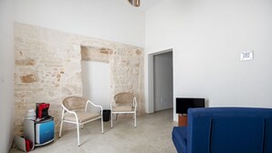 Una habitación con pared de piedra, dos sillas de mimbre, un sofá azul, un televisor y una máquina de café.