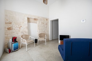 A room with a stone wall, two wicker chairs, a blue sofa, a television, and a coffee machine. - Spacious double bedroom with living area and private bathroom, ideal for two, located within Trulli Italia, a complex of trulli with a shared garden. Surrounded by greenery, the accommodation is located in Selva di Fasano, a quiet and verdant hillside ha (Selva di Fasano)