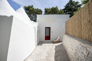 A narrow courtyard with a red door, a white wall, and a wooden fence. - Spacious double bedroom with living area and private bathroom, ideal for two, located within Trulli Italia, a complex of trulli with a shared garden. Surrounded by greenery, the accommodation is located in Selva di Fasano, a quiet and verdant hillside ha (Selva di Fasano)