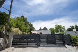 Ein verschlossenes Tor mit einem weißen Gebäude im Hintergrund, umgeben von Bäumen.