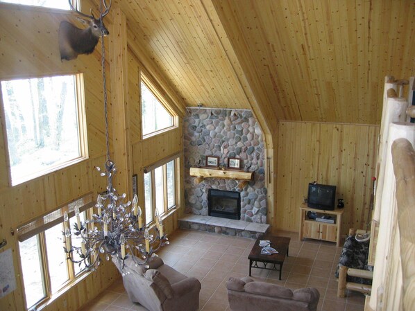 A wooden interior with a stone fireplace, two sofas, a coffee table, and a television.