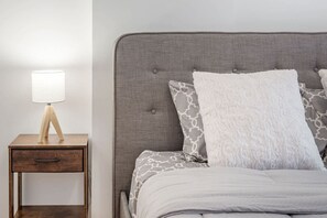 A bed with a grey upholstered headboard, a bedside table with a lamp, and patterned pillows. - 1 BR Old Port| Basilica (Montréal)