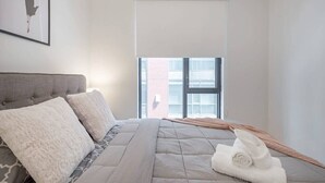 Ein Schlafzimmer mit einem Bett, Kissen, einer Decke, einem Fenster und einem Bild an der Wand.