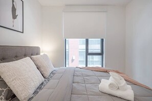 Un dormitorio con una cama, almohadas, un edredón, una ventana y un cuadro en la pared.