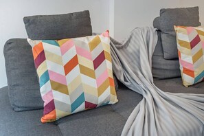Un canapé gris agrémenté de deux coussins aux motifs colorés en forme de chevrons et d’un plaid gris.