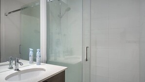 Ein modernes Badezimmer mit einer Duschkabine aus Glas, einem weißen Waschbecken mit zwei Wasserhähnen und zwei Seifenspendern.