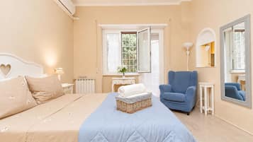 Een slaapkamer met een bed, een blauwe fauteuil, een nachtkastje, een dressoir, een raam en een spiegel.