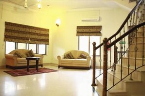 A living room with two sofas, a coffee table, and a staircase with a wooden railing. - Comfort Residency (Islamabad)
