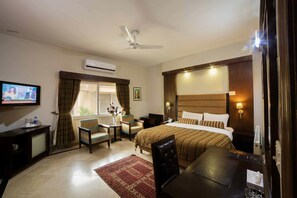 A hotel room with a bed, a desk, a chair, a television, and an air conditioning unit. - Comfort Residency (Islamabad)