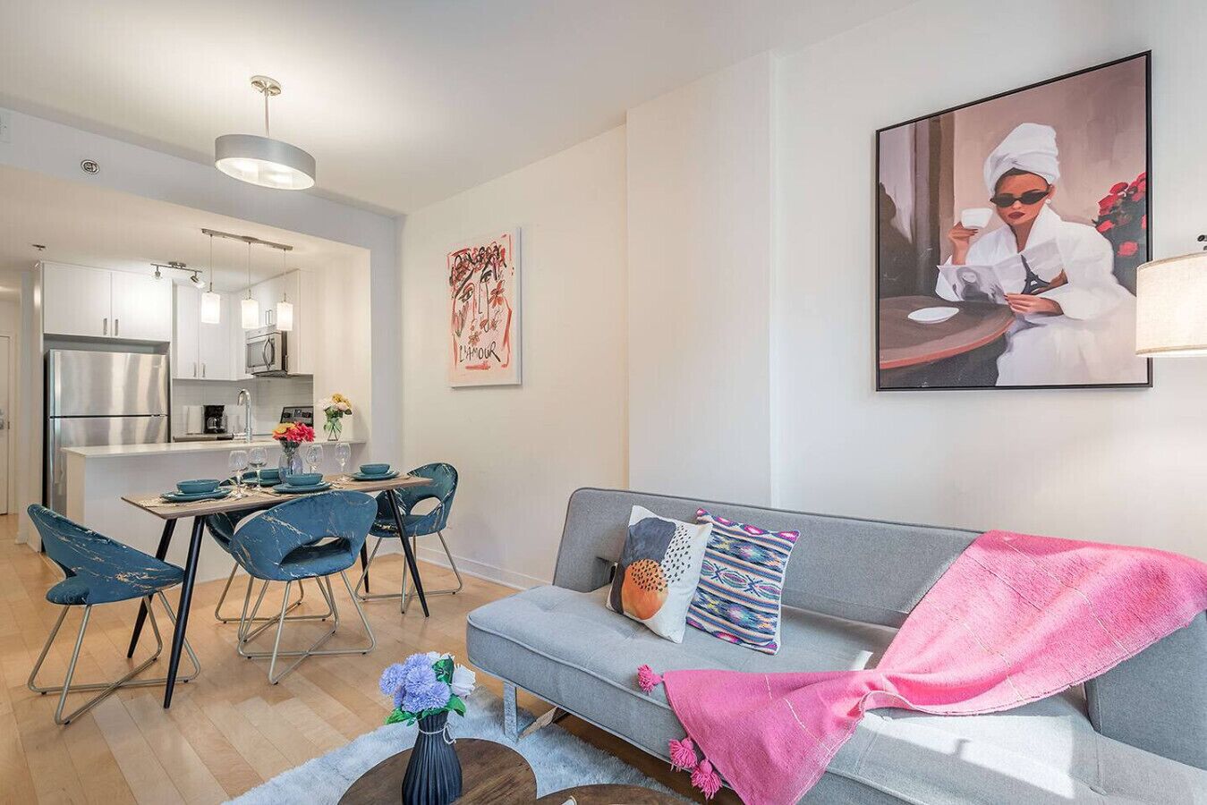 A modern living room with a grey sofa, blue chairs, a dining table, and a kitchen in the background.