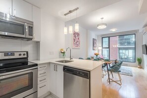 A modern kitchen with stainless steel appliances, a dishwasher, and a dining area with bar stools. - 1 BR Old Port| Basilica (Montreal)