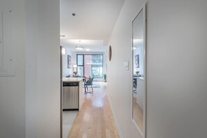 A modern kitchen with a dishwasher, a dining area with a chair, and a hallway leading to a living space. - 1 BR Old Port| Basilica (Montreal)