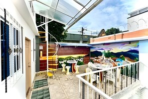 Ein Wohngebiet mit einer Treppe, die zu einem Balkon führt, einer Wandmalerei an der Wand und einer kleinen Sitzgelegenheit im Freien.