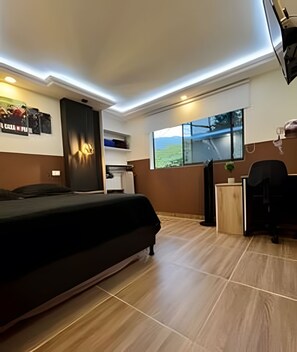 Ein Schlafzimmer mit Bett, Schreibtisch, Stuhl und einem Fenster mit Blick auf Grünflächen.