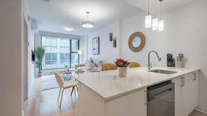 Una cocina moderna con una isla central, una zona de comedor con sillas, un ventanal grande y una lámpara colgante.