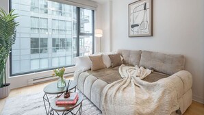 Una sala de estar moderna con un sofá, una mesita de centro, una planta en maceta y una ventana con vista a la ciudad.