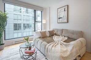 Una sala de estar moderna con un sofá, una mesita de centro, una planta en maceta y una ventana con vista a la ciudad.