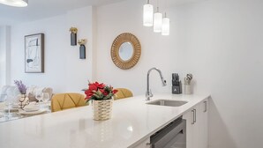 Una cocina moderna con encimera blanca, pileta de acero inoxidable y lavavajillas integrado.