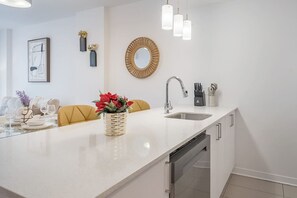 Una cocina moderna con encimera blanca, pileta de acero inoxidable y lavavajillas integrado.