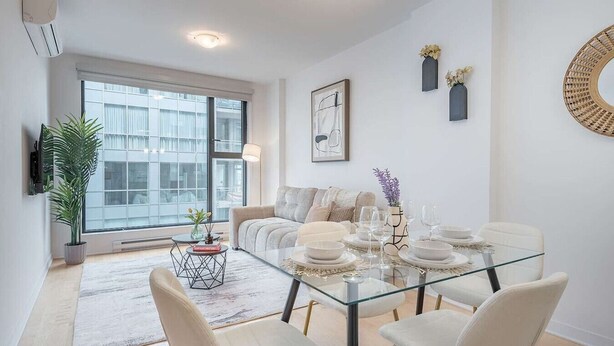 Una sala de estar moderna con una mesa de comedor de vidrio, sillas blancas, un sofá y un ventanal grande.