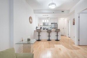 Cozinha moderna com armários brancos, uma ilha central com banquetas e uma mesa de jantar com um vaso de flores.
