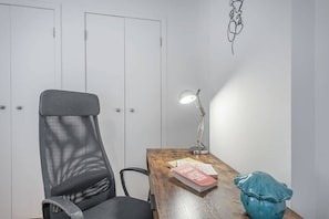 A room with a wooden desk, a black mesh office chair, a desk lamp, a blue vase, and closed white doors. - 1 BR Old Port| Basilica (Montreal)