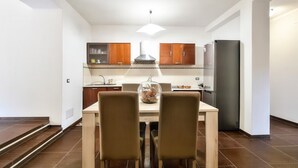 A modern kitchen with wooden cabinets, a dining table with two chairs, and a refrigerator. - B&B in the heart of Loceri - Apartment (Loceri)
