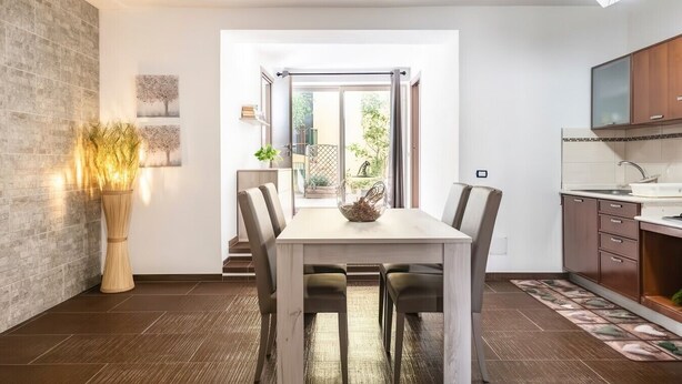 A modern dining area with a wooden table, chairs, and a vase of dried plants. - B&B in the heart of Loceri - Apartment (Loceri)
