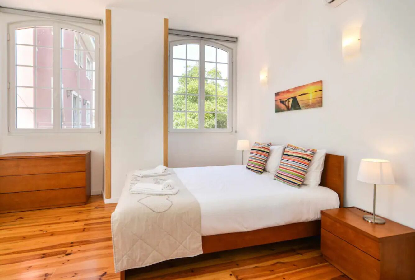 Un dormitorio con cama, mesitas de noche, una ventana y un cuadro en la pared.