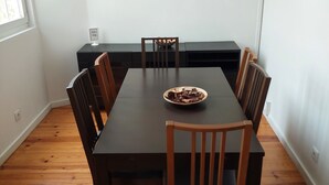 A dining area with a long table, wooden chairs, and a painting of a sunset over the ocean. - Lightoasis Oeiras 2 (Oeiras)