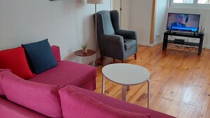 A living room with a pink sofa, a grey armchair, a small round table, and a TV on a stand. - Lightoasis Oeiras 2 (Oeiras)