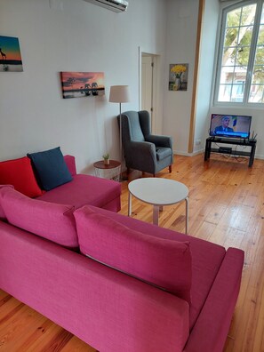A living room with a pink sofa, a grey armchair, a small round table, and a TV on a stand. - Lightoasis Oeiras 2 (Oeiras)