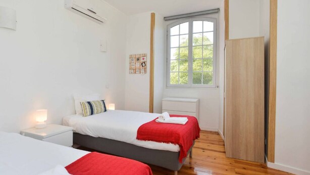 A hotel room with two beds, a window with a view, a wardrobe, and a bedside table with a lamp. - Lightoasis Oeiras 2 (Oeiras)