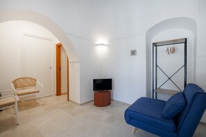 Ein Zimmer mit einem blauen Sofa, einem weißen Sessel, einem Fernseher auf einem Holzständer und einem Wäscheständer.