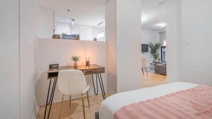 Ein Schlafzimmer mit Bett, Schreibtisch mit Stuhl, einem kleinen Tisch mit Lampe und einem Fernseher im Hintergrund.
