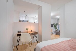 Ein Schlafzimmer mit Bett, Schreibtisch mit Stuhl, einem kleinen Tisch mit Lampe und einem Fernseher im Hintergrund.