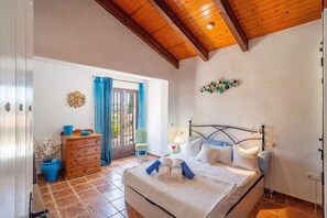 Ein Schlafzimmer mit Bett, Holzkommode, blauen Vorhängen und Blick durch ein Fenster.