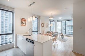 Eine moderne Küche mit Kochinsel, ein Essbereich mit Tisch und Stühlen sowie große Fenster mit Blick auf die Stadt.