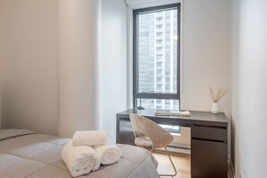 Un dormitorio con cama, escritorio, silla y ventana con vista a la ciudad.