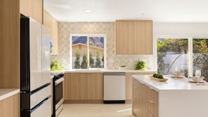 Cocina moderna con armarios de madera, lavavajillas y un amplio ventanal con vistas a un paisaje montañoso.