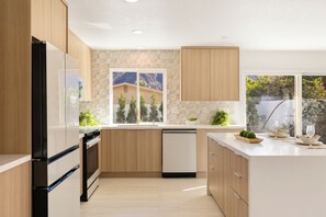 A modern kitchen with wooden cabinets, a dishwasher, and a large window overlooking a mountainous landscape. - New Luxury House Near Golf, Trails & Restaurants. Voted "Top 10 Best New Houses" (La Quinta)