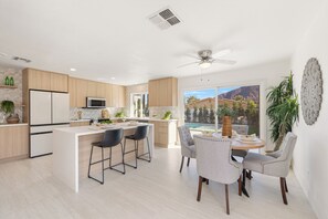 A modern kitchen with a central island, bar stools, and a dining area with a round table and chairs. - New Luxury House Near Golf, Trails & Restaurants. Voted "Top 10 Best New Houses" (La Quinta)