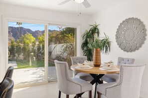 A dining area with a table set for four, surrounded by chairs, a large vase, and a decorative wall piece. - New Luxury House Near Golf, Trails & Restaurants. Voted "Top 10 Best New Houses" (La Quinta)