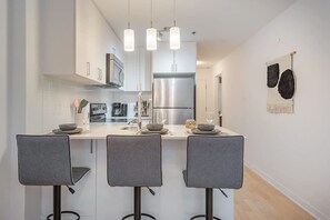 Una cucina moderna con isola centrale, sgabelli da bar, elettrodomestici in acciaio inossidabile e illuminazione a sospensione.