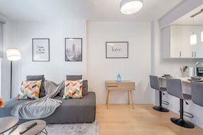 Ein modernes Wohnzimmer mit einer Couch, einem kleinen Tisch und einer Küchenzeile mit Barhocker.